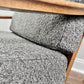 Close-up of a gray boucle upholstered chair with a warm medium-brown wooden frame and armrest.