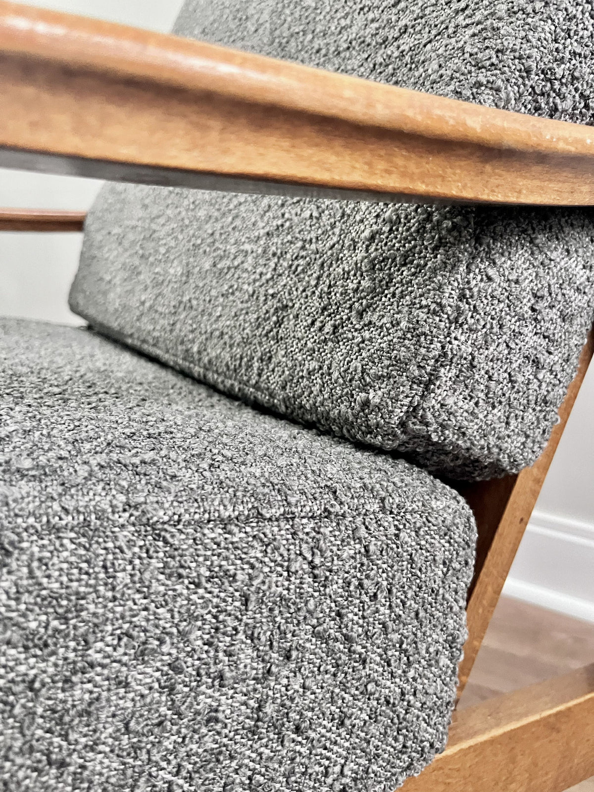 Close-up of a gray boucle upholstered chair with a warm medium-brown wooden frame and armrest.