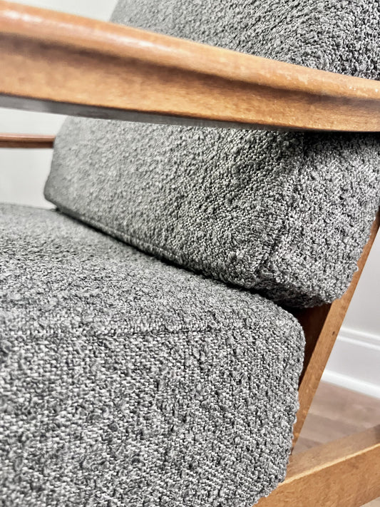 Close-up of a gray boucle upholstered chair with a warm medium-brown wooden frame and armrest.