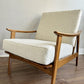 A mid-century modern accent chair with a warm medium-brown wooden frame and textured cream bouclé upholstery.