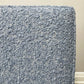 Close-up of a textured woven fabric in light blue boucle, showing the detailed boucle-like weave against a neutral wall background.