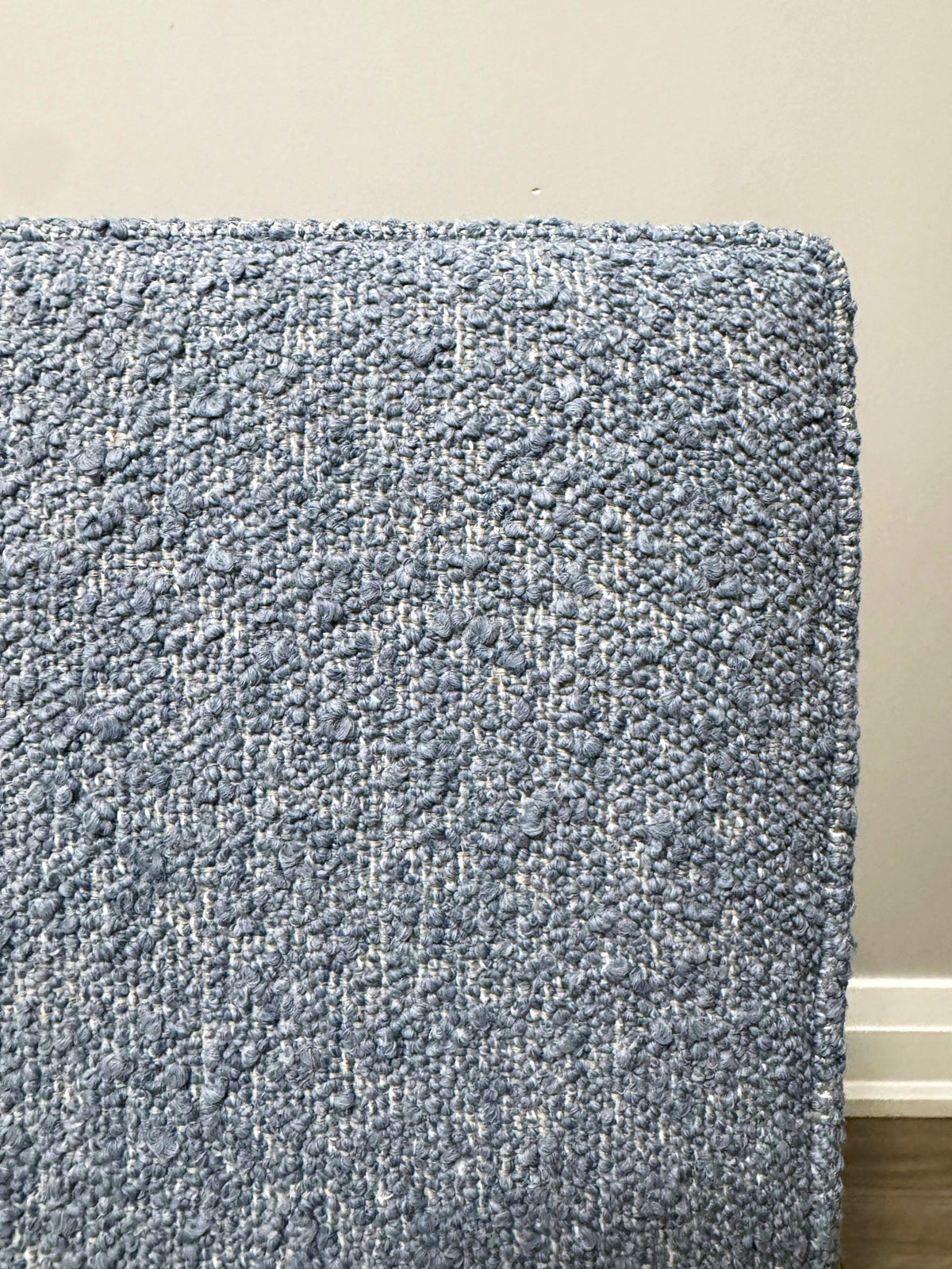 Close-up of a textured woven fabric in light blue boucle, showing the detailed boucle-like weave against a neutral wall background.