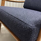 Close-up of a mid-century modern armchair with a dark navy blue textured bouclé fabric seat cushion and a light natural wood frame.