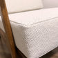 Close-up of a woven off-white fabric cushion on a wooden chair, showing the texture and corner detail.