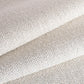 A close-up of a woven fabric texture in a warm off-white, folded diagonally to show the material's texture and drape.