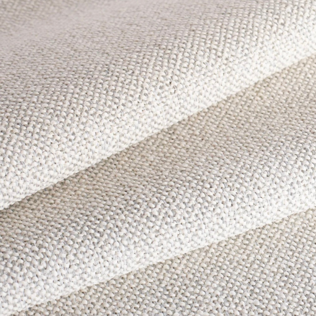 A close-up of a woven fabric texture in a warm off-white, folded diagonally to show the material's texture and drape.