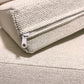 Close-up of a cream woven fabric cushion with a white zipper pull, resting on a matching cushion.