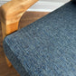 Close-up of a blue textured woven upholstery fabric on an armchair, with a light natural wood armrest and wooden floor visible.