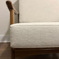 Close-up of a mid-century modern armchair with textured off-white woven upholstery and a warm medium-brown wooden frame.