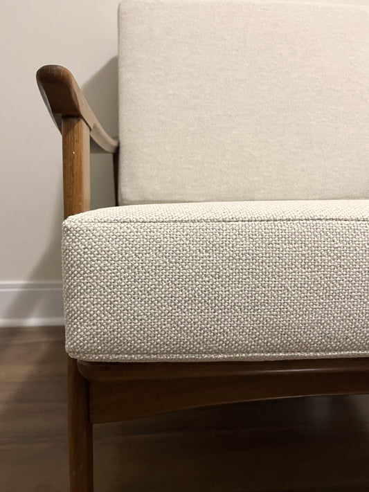 Close-up of a mid-century modern armchair with textured off-white woven upholstery and a warm medium-brown wooden frame.